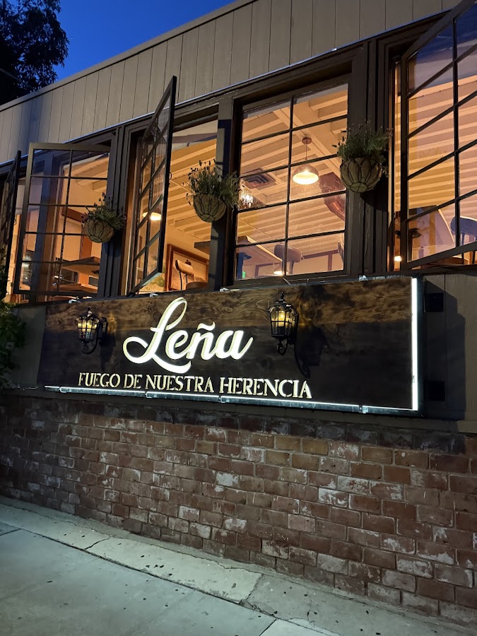 Leña Restaurant at dusk: the illuminated Leña sign, Fuego de Nuestra Herencia, above the brick wall at 2431 Central Ave, Alameda